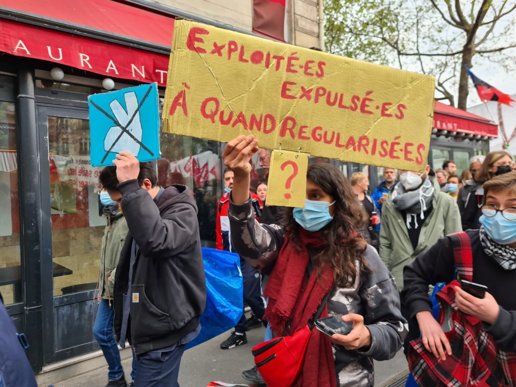 Photo de la manifestation avec la pancarte : "Exploité.e.s expulsé.e.s, à quand régularisé.e.s ?"