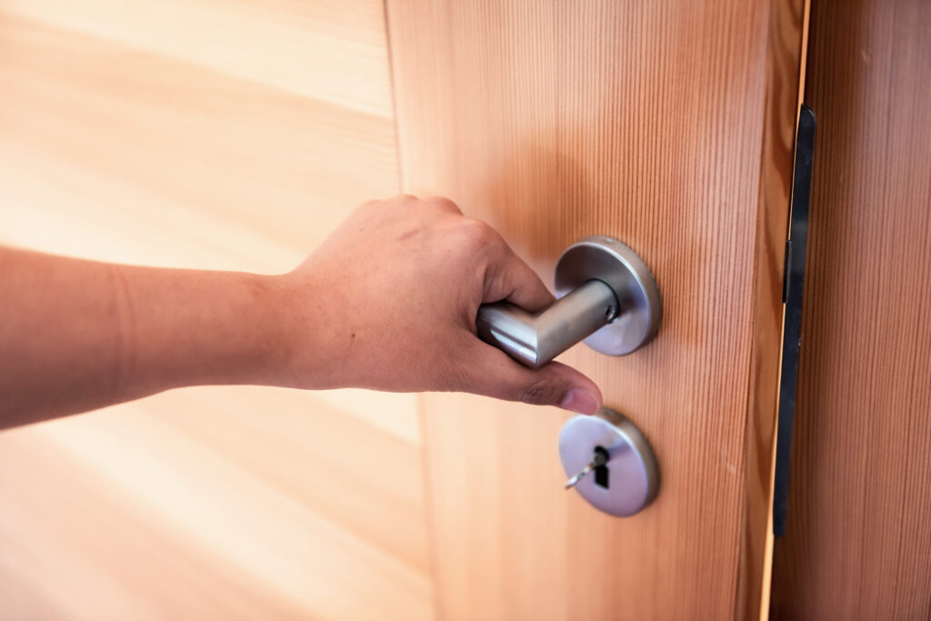 Une main tient la poignée d'une porte pour la fermer.